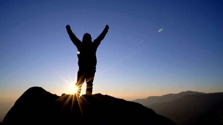 4K RT WS Silhouette man standing on mountain and raising arms towards sunrise sky. Successful concept.